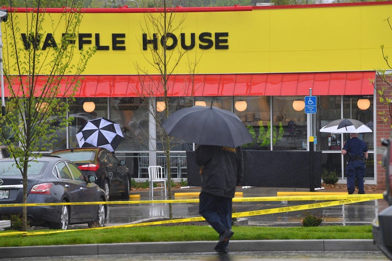 Caution tape and police officers holding umbrellas are seen outside the Waffle House.